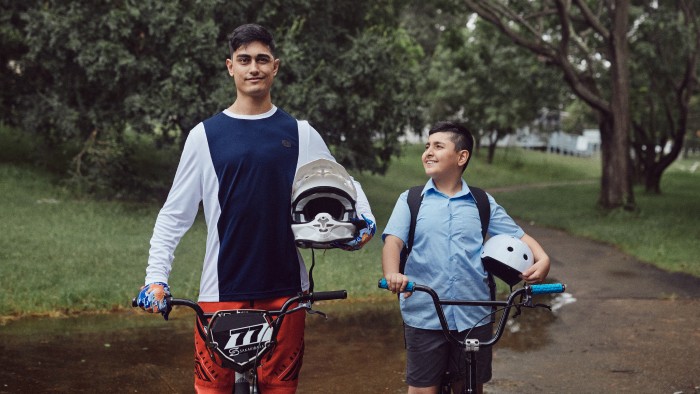 Two young men standing with their bikes and holding helmets on a trail.